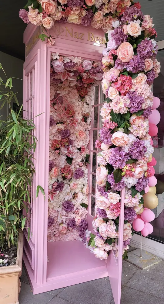 Die rosa Telefonzelle von innen: eine Wand aus Rosen, Hortensien und Pfingstrosen in Rosa, Apricot und Flieder